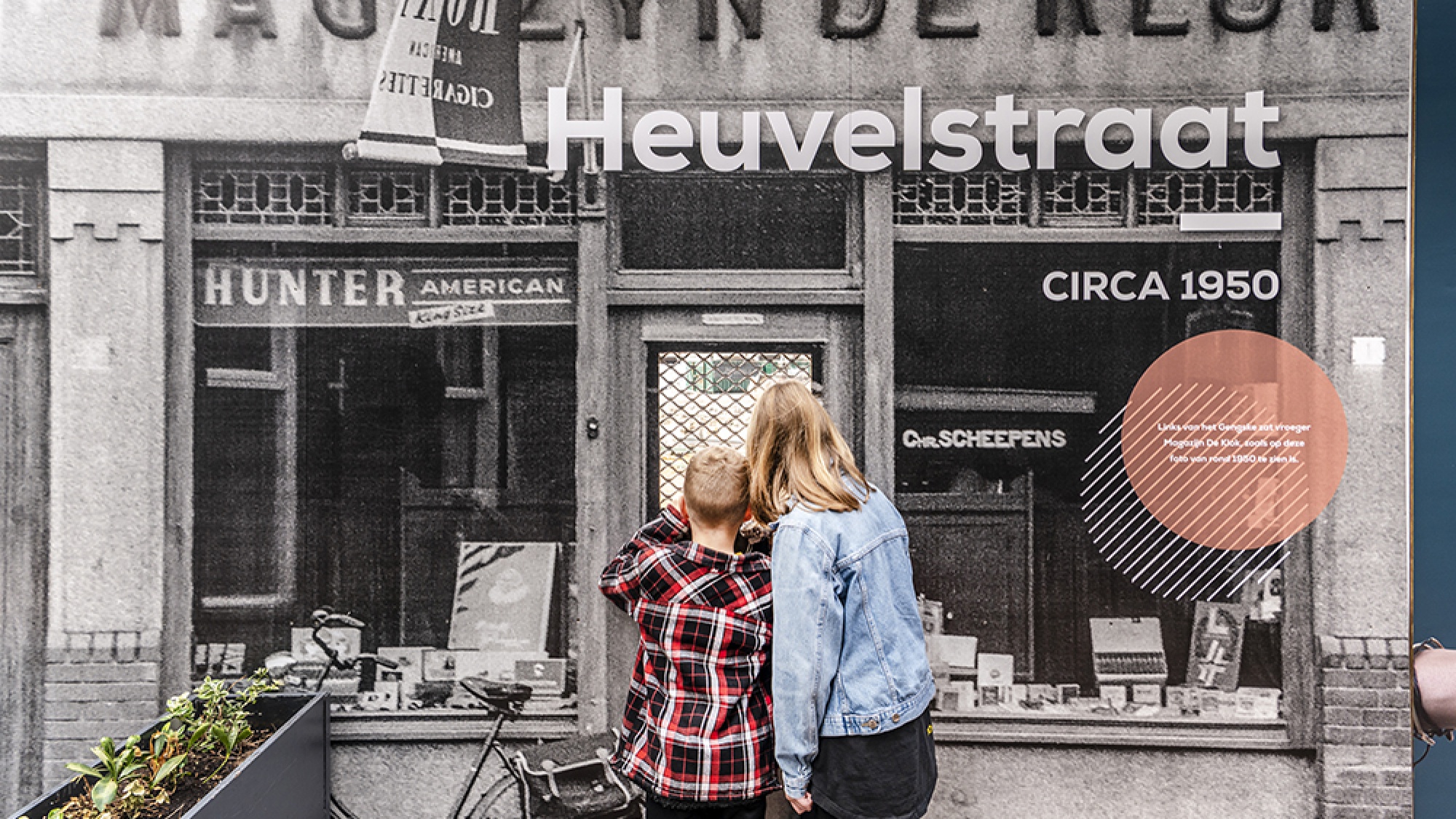 Vrouw en jongetje kijken samen door het kijkgat naar het bouwterrein.