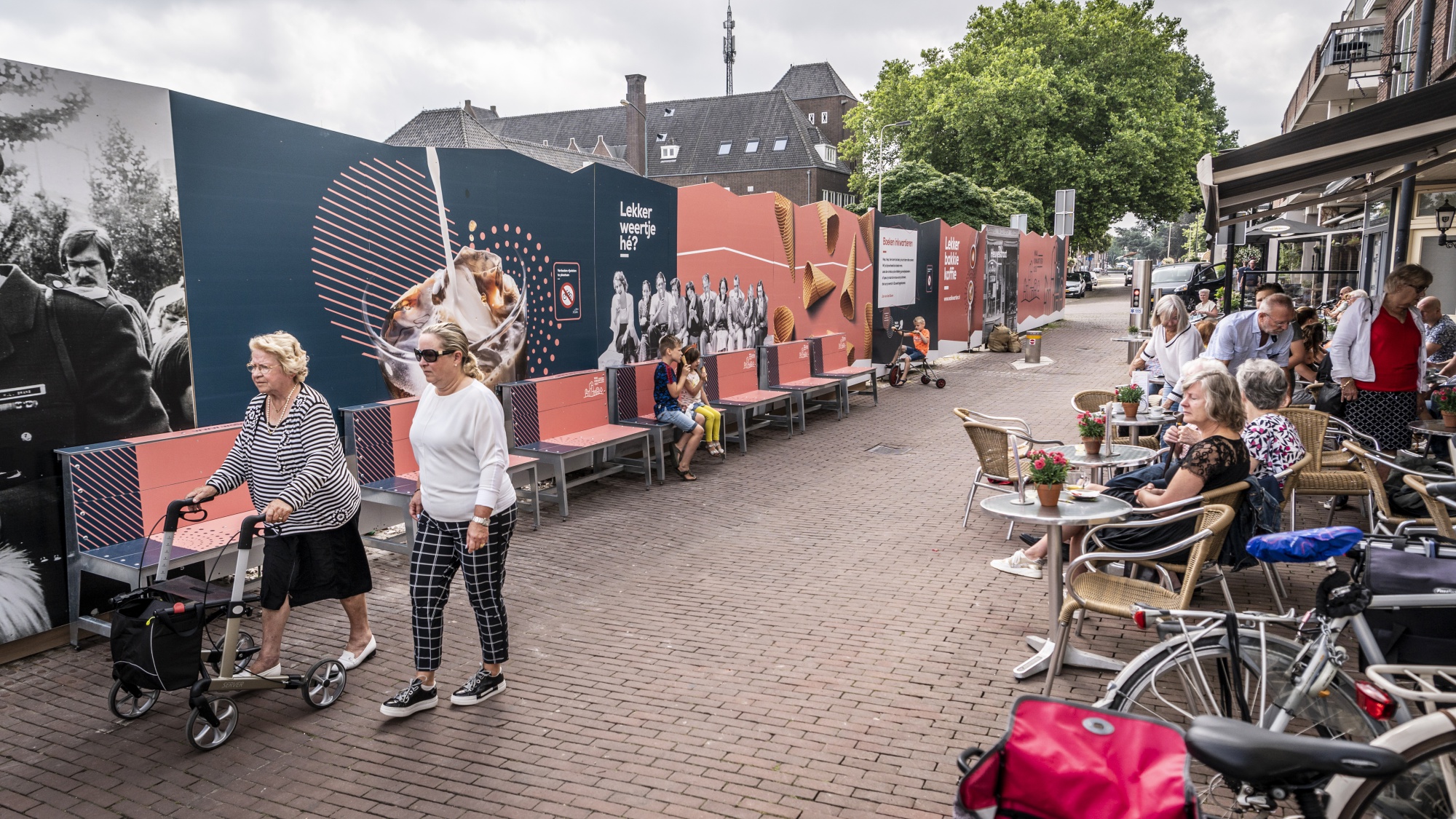 Links de perimeter en rechts een terras dat uitkijkt op de perimeter met mensen die er tussendoor wandelen. 