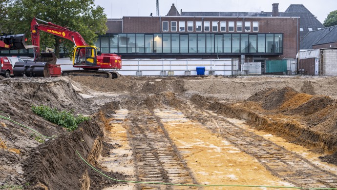 Kuil in grond. Links een graafmachine en op de achtergrond het TBL.